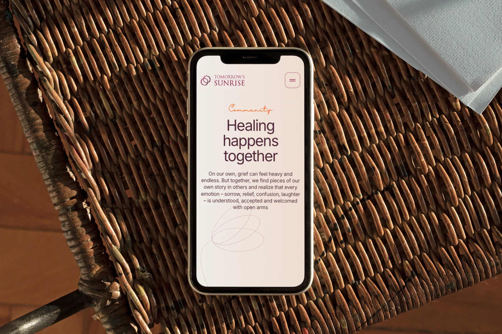 The Tomorrow’s Sunrise homepage on a phone, resting on a wicker chair