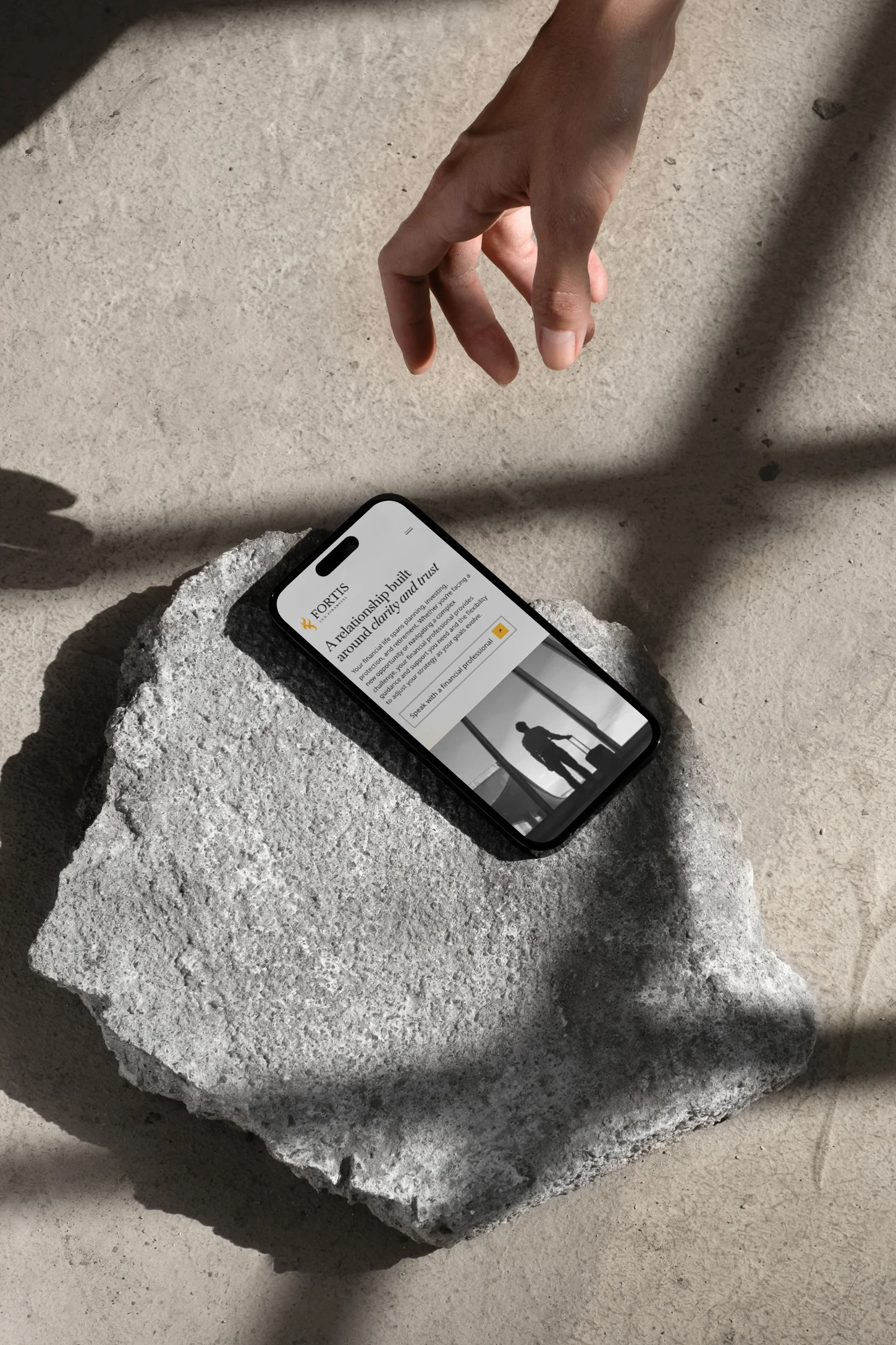 The Fortis Lux who we serve page on a phone, resting on stone