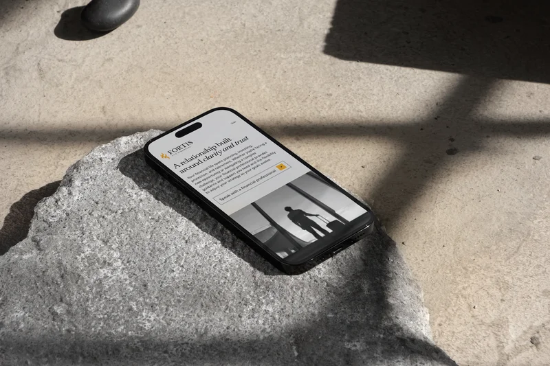 The Fortis Lux who we serve page on a phone, resting on a rock